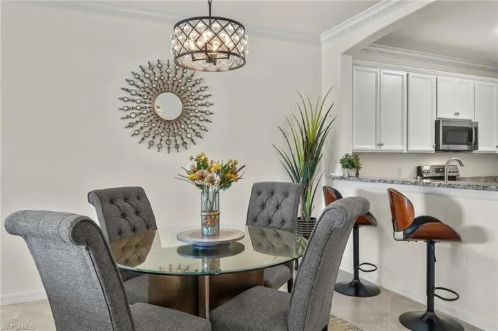 Fully furnished dining room with crown molding, ornamental chandelier, and tile floors.