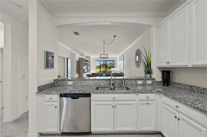 Kitchen with granite countertops, white cabinetry, stainless steel dishwasher, ornamental molding and lake views.