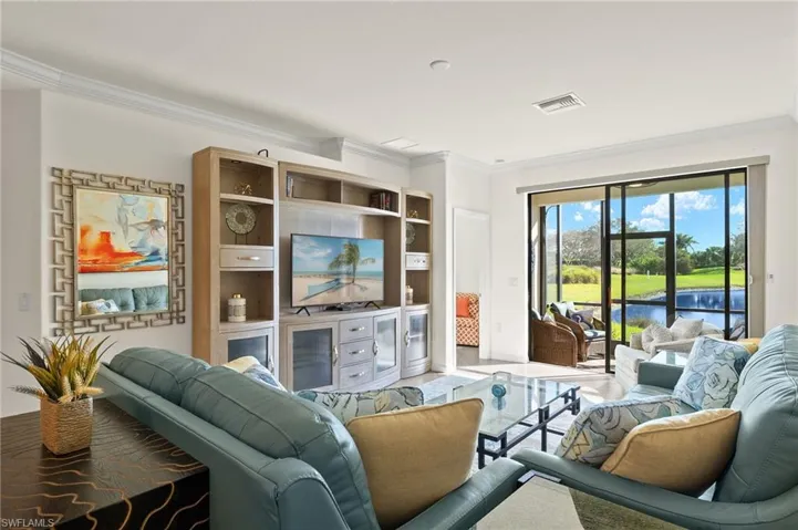 Fully furnished living room featuring an entertainment center, crown molding and tranquil lake views.