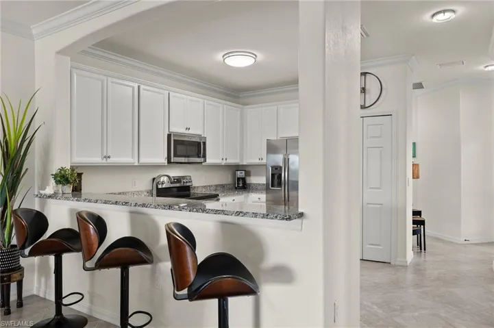 Bar area, and kitchen with granite countertops, stainless steel appliances, and white cabinetry