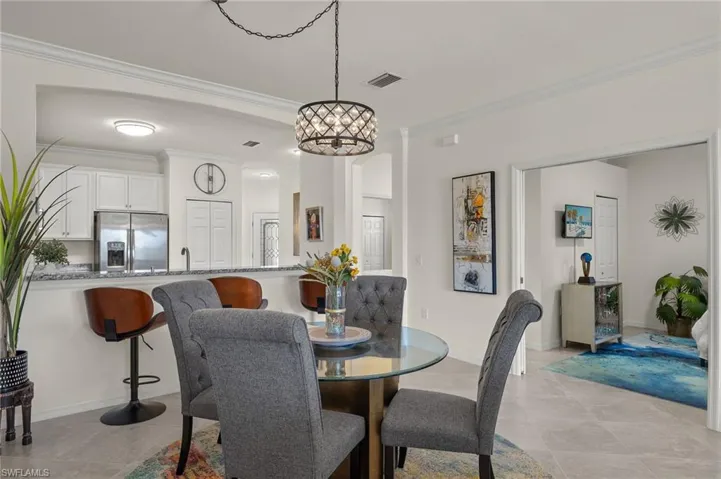 Fully furnished dining room with crown molding, ornamental chandelier, and tile floors.