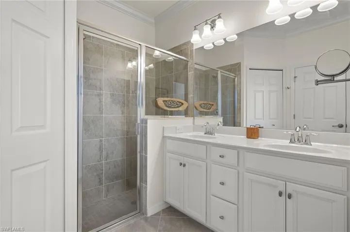 Primary Bathroom featuring double vanity, a walk-in tiled shower, ornamental molding, tile floor and a private water closet.
