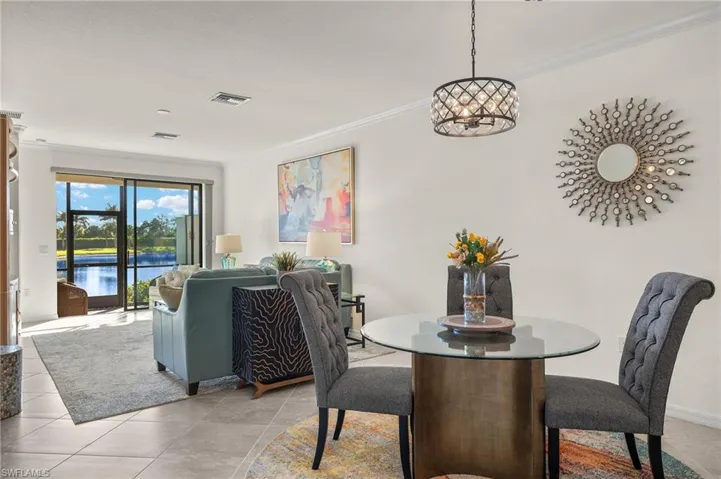 Fully furnished dining room with crown molding, ornamental chandelier, tile floors and peaceful water views.