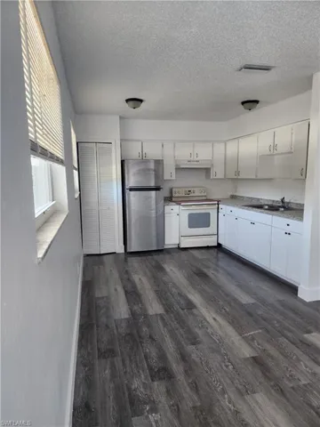 Kitchen featuring electric stove, freestanding refrigerator, white cabinetry, dark wood-type flooring, and a textured ceiling