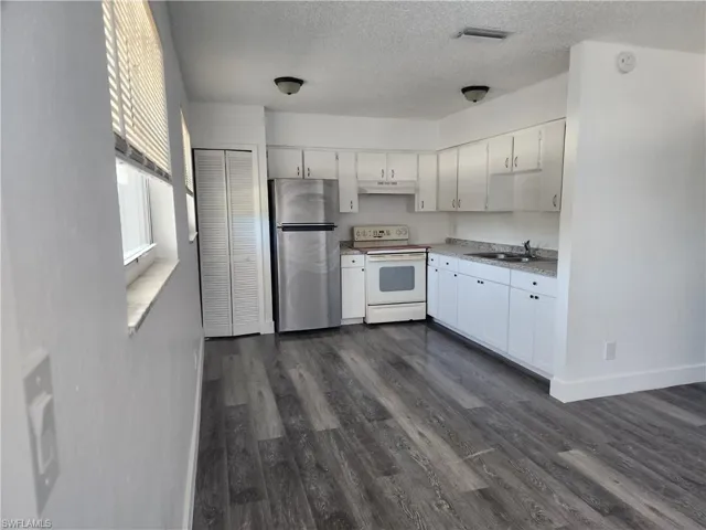 Kitchen featuring white electric stove, freestanding refrigerator, light countertops, white cabinets, and a textured ceiling