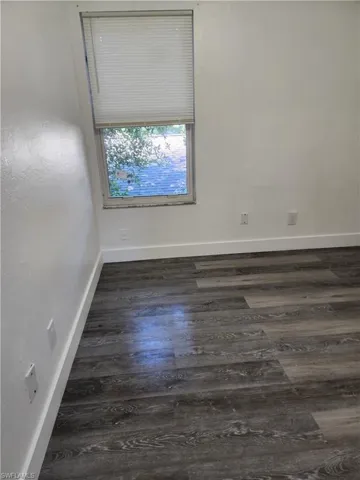 Unfurnished room featuring dark wood-style floors and baseboards