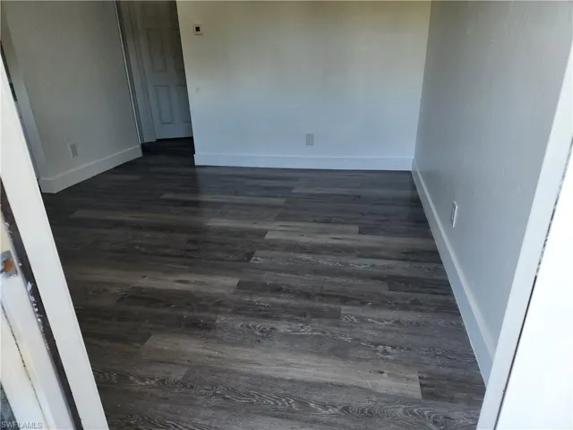 Unfurnished room with dark wood-style floors and baseboards