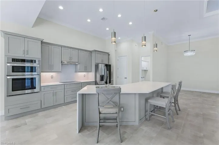 Kitchen with hanging light fixtures, gray cabinetry, stainless steel appliances, an island with sink, and tasteful backsplash