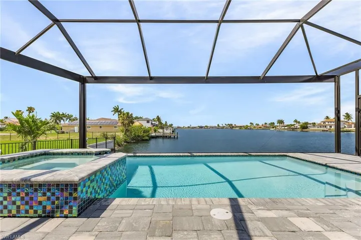 View of swimming pool with a water view, glass enclosure, and an in ground hot tub