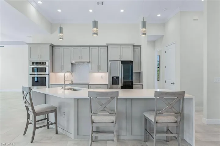 Kitchen featuring stainless steel appliances, an island with sink, decorative light fixtures, sink, and light tile floors