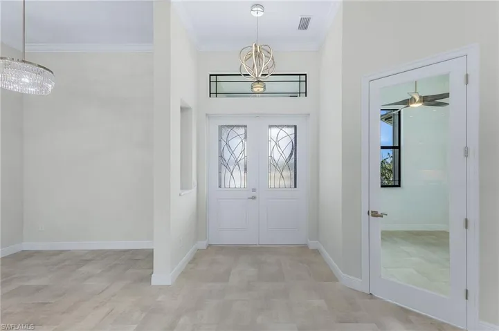 Entrance foyer with ceiling fan with notable chandelier, french doors, and ornamental molding
