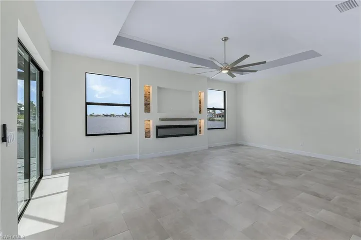 Unfurnished living room featuring a healthy amount of sunlight, ceiling fan, and a raised ceiling