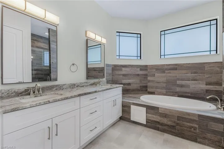 Bathroom with dual sinks, tile walls, tile floors, tiled bath, and large vanity