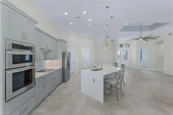 Kitchen featuring ceiling fan, an island with sink, stainless steel appliances, hanging light fixtures, and sink