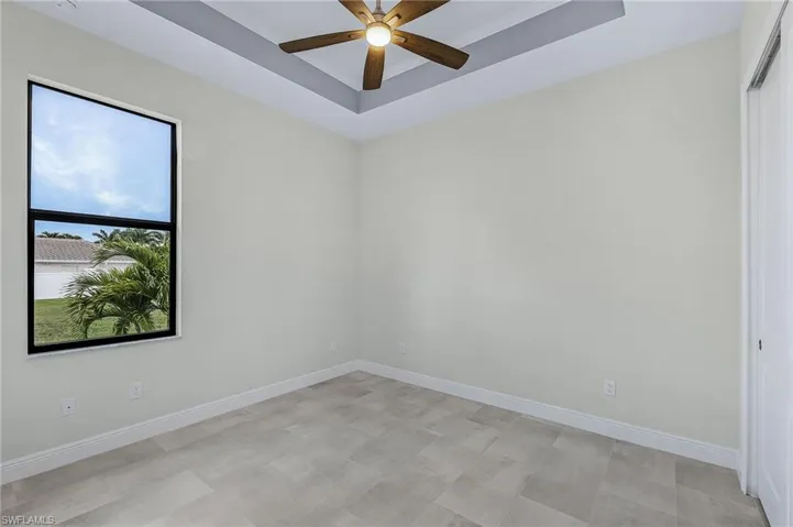 Empty room featuring light tile flooring, ceiling fan, and a tray ceiling