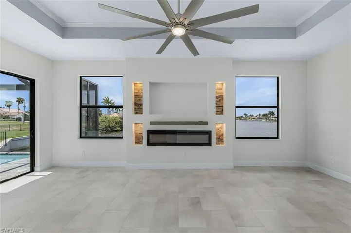 Unfurnished living room featuring ceiling fan, a raised ceiling, and crown molding