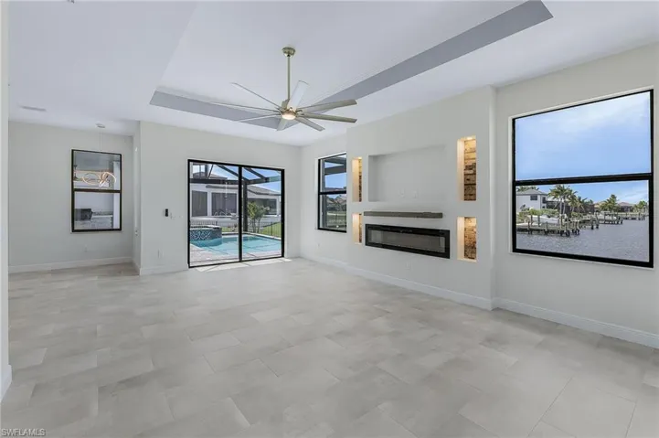 Unfurnished living room with ceiling fan, a water view, a tray ceiling, and light tile floors