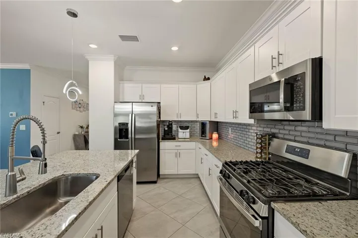 Kitchen featuring light stone counters, a sink, white cabinetry, appliances with stainless steel finishes, and pendant lighting