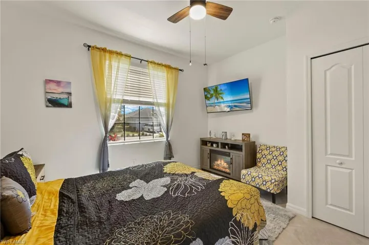 Bedroom with light tile patterned floors, ceiling fan, and a glass covered fireplace