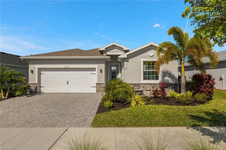 Ranch-style house with decorative driveway, stucco siding, an attached garage, a front yard, and stone siding