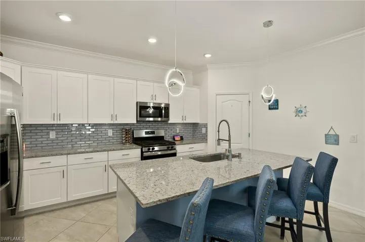 Kitchen with decorative light fixtures, stainless steel appliances, a kitchen island with sink, white cabinets, and a sink