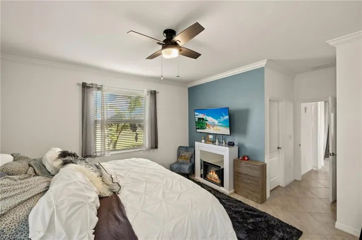 Bedroom with light tile patterned floors, ornamental molding, a glass covered fireplace, ceiling fan, and baseboards