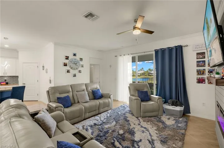 Living room featuring light tile patterned floors, baseboards, visible vents, a ceiling fan, and crown molding
