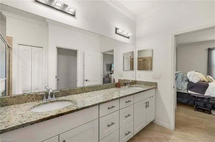 Ensuite bathroom with double vanity, a closet, ornamental molding, and a sink