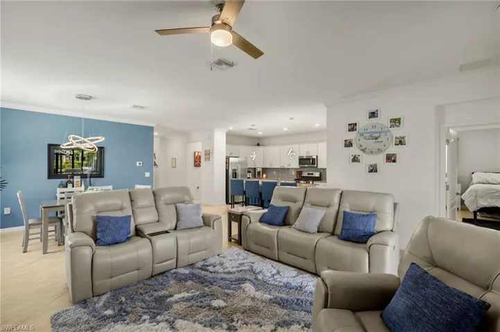 Living area featuring light tile patterned floors, ceiling fan, visible vents, and ornamental molding