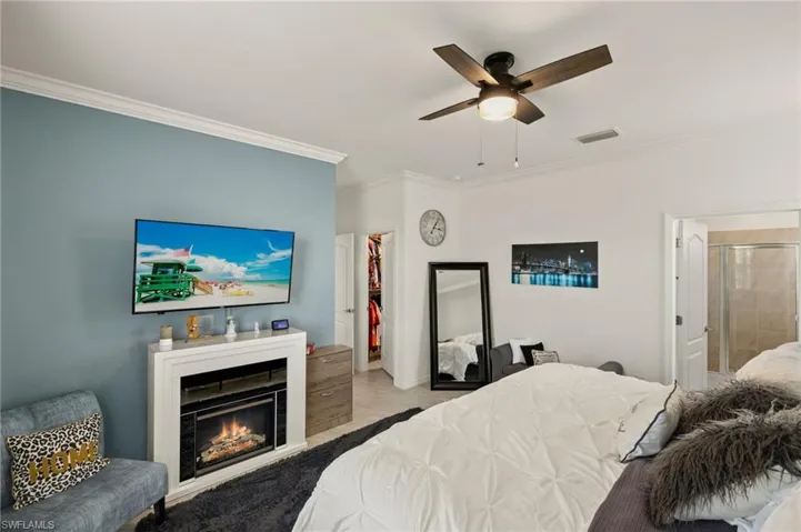 Bedroom featuring ceiling fan, a glass covered fireplace, visible vents, and crown molding