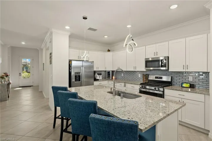 Kitchen featuring a kitchen island with sink, stainless steel appliances, a sink, white cabinetry, and hanging light fixtures
