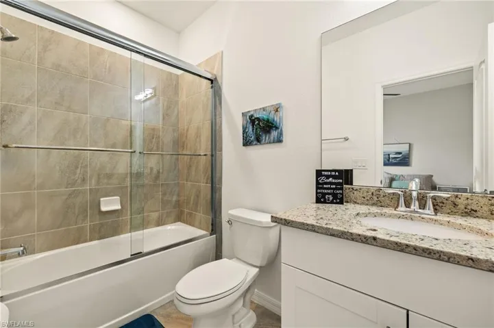 Bathroom with baseboards, vanity, toilet, and bath / shower combo with glass door
