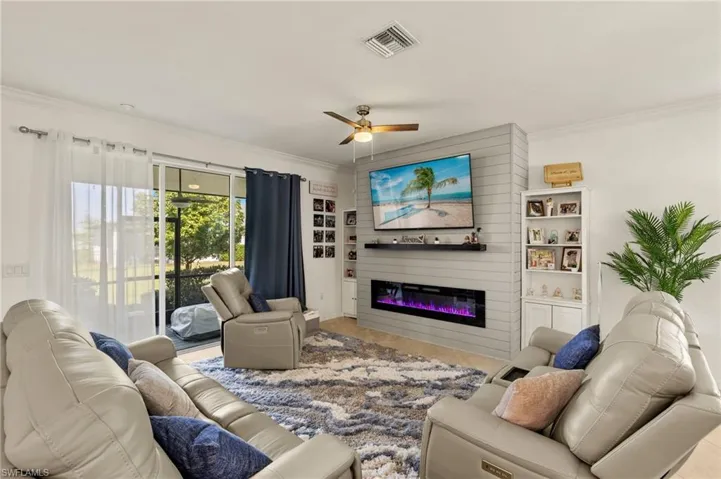 Living area featuring ornamental molding, a glass covered fireplace, visible vents, and a ceiling fan