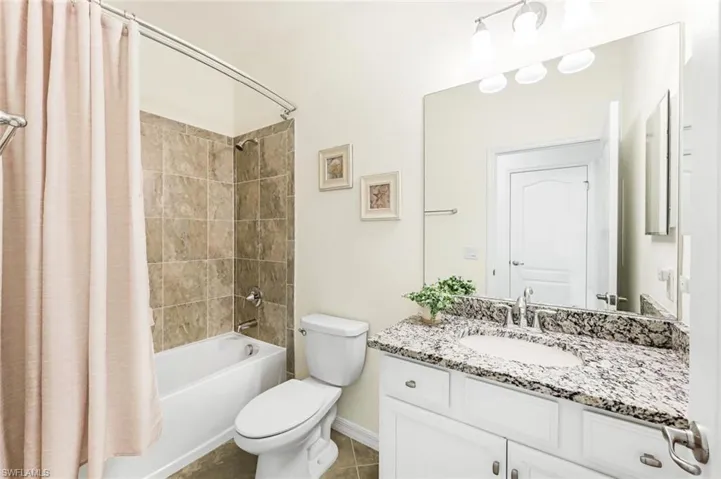Full bathroom with shower / tub combo with curtain, vanity, toilet, and tile patterned floors