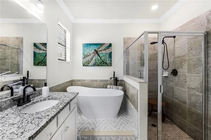 Bathroom featuring tile walls, independent shower and bath, vanity, and crown molding