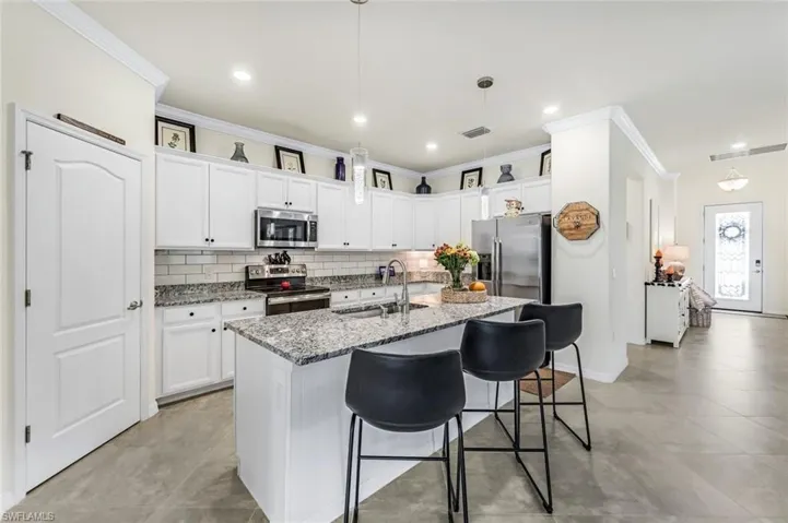 Kitchen featuring sink, white cabinetry, hanging light fixtures, appliances with stainless steel finishes, and crown molding
