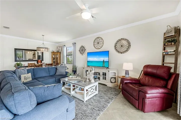 Living room featuring ceiling fan with notable chandelier, light tile patterned floors, and crown molding
