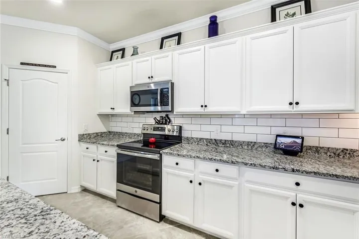 Kitchen featuring light stone countertops, white cabinetry, appliances with stainless steel finishes, and tasteful backsplash