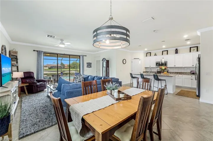Dining space with light tile patterned floors, sink, ceiling fan with notable chandelier, and ornamental molding