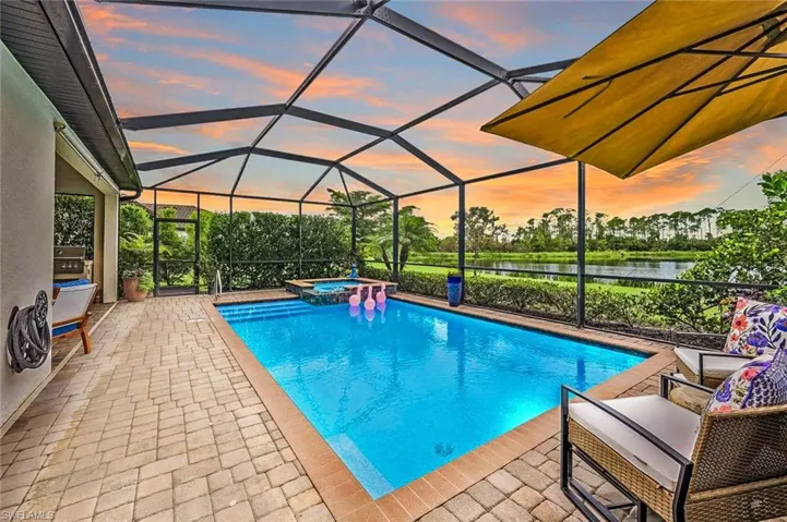 Pool at dusk with a lanai, a water view, and a patio area