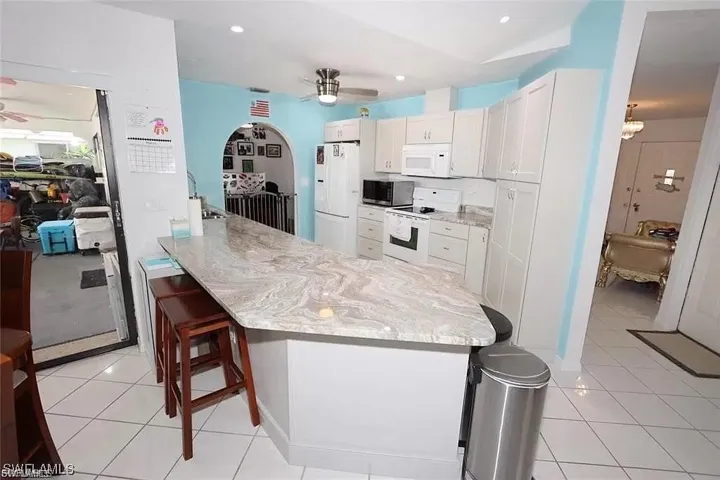 Kitchen with a ceiling fan, white appliances, a kitchen bar, white cabinetry, and recessed lighting
