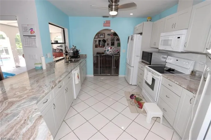 Kitchen featuring white appliances, white cabinetry, a peninsula, light tile patterned floors, and light stone counters