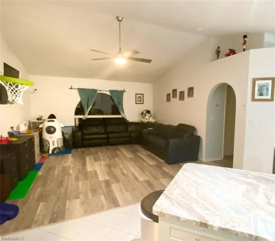 Living area featuring vaulted ceiling, arched walkways, light wood-type flooring, and ceiling fan