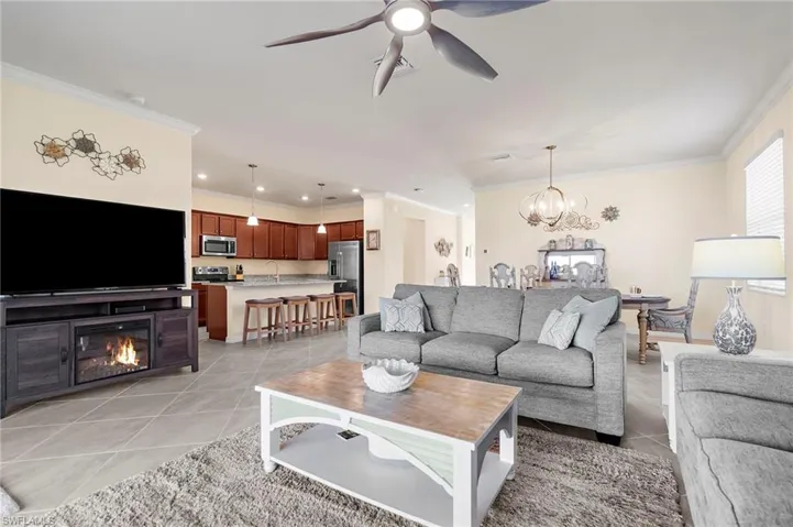 Living room featuring sink, light tile patterned flooring, ceiling fan with notable chandelier, and ornamental molding