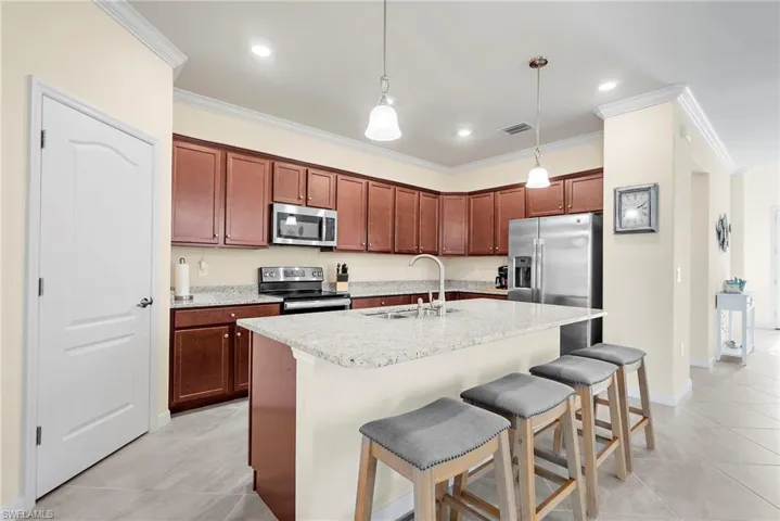 Kitchen with a kitchen island with sink, hanging light fixtures, sink, crown molding, and appliances with stainless steel finishes