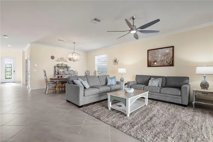 Living room featuring light tile patterned floors, ceiling fan with notable chandelier, a wealth of natural light, and crown molding