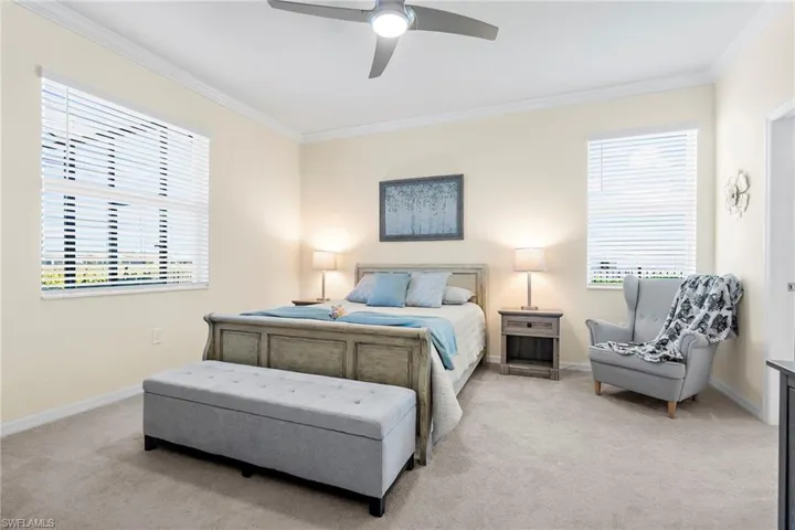 Bedroom with light colored carpet, multiple windows, ornamental molding, and ceiling fan