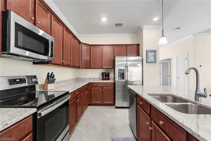 Kitchen with sink, stainless steel appliances, light stone counters, decorative light fixtures, and ornamental molding