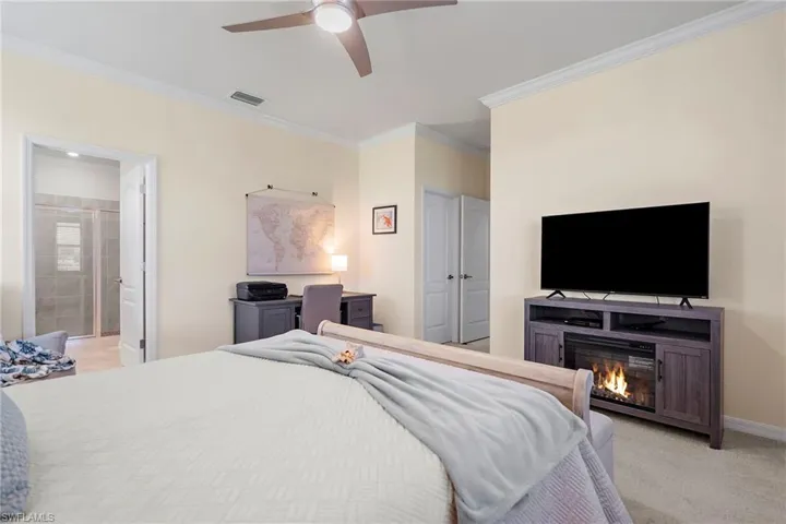 Carpeted bedroom featuring ceiling fan, crown molding, and ensuite bath