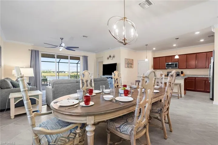 Dining room with ceiling fan with notable chandelier, ornamental molding, and light tile patterned floors